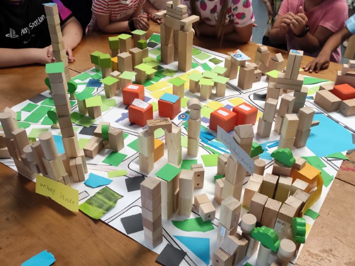 Das Foto zeigt ein von Kindern gebautes Stadtmodell aus Bauklötzen und bunten Papierelementen