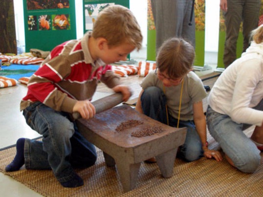 Kinder reiben Kakaonibs an mexikanischen Reibsteinen